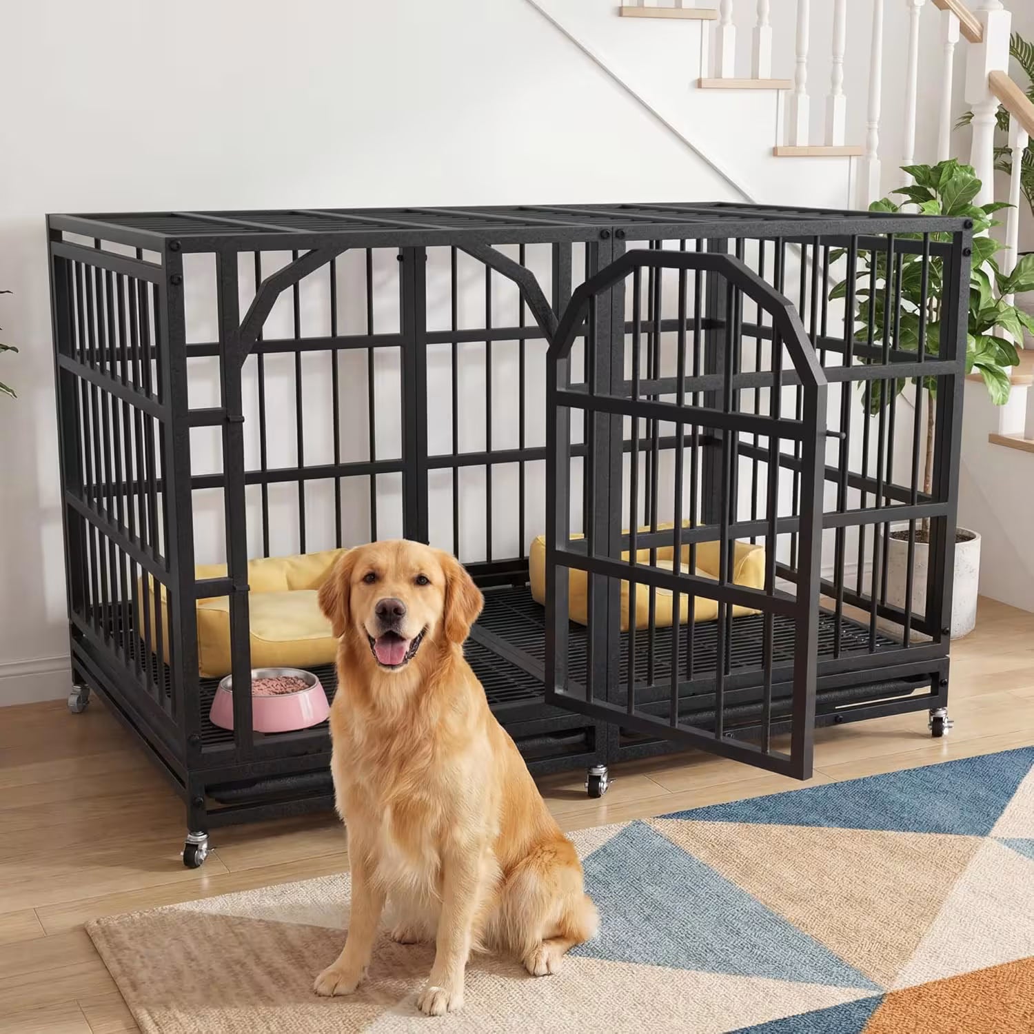 A golden retriever dog sits in front of a large black metal pet crate with an open door, placed in a bright home interior with a staircase, plant, rug, and pet bed visible.